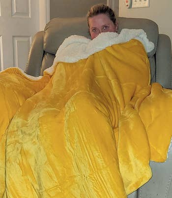 Person wrapped in a large yellow blanket, seated on a chair, peering over the top