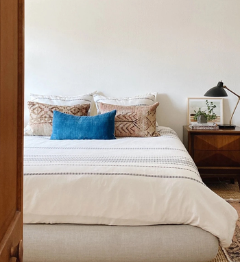 the beige bed frame topped with a mattress, comforter, and pillows