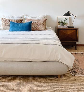 the beige bed frame topped with a mattress, comforter, and pillows