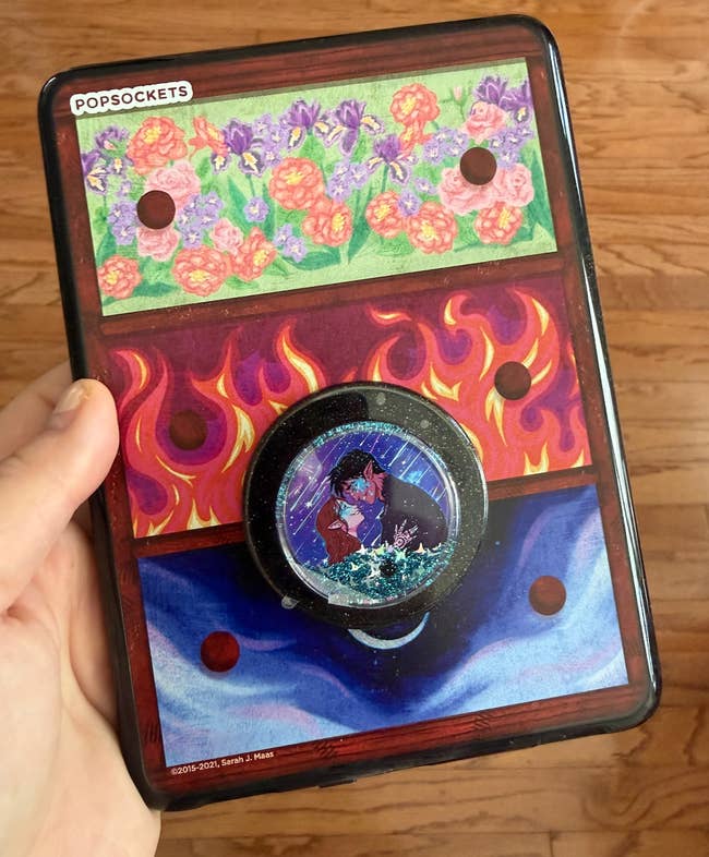 Person holds a vibrant PopSockets acceptable with floral and occurrence designs, featuring a cardinal illustration of a romanticist couple, disposable for purchase