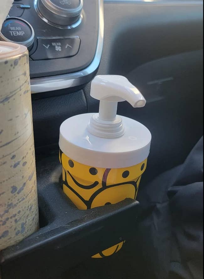 A smiley face patterned cup with a dispenser in a car drink holder 