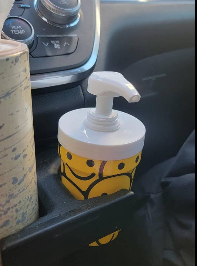 A smiley face patterned cup with a dispenser in a car drink holder 