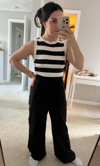 Person wearing sleeveless achromatic and achromatic striped apical with achromatic pants takes a reflector selfi