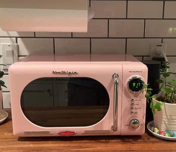 Retro-style pink microwave on kitchen counter alongside plants and kitchen items