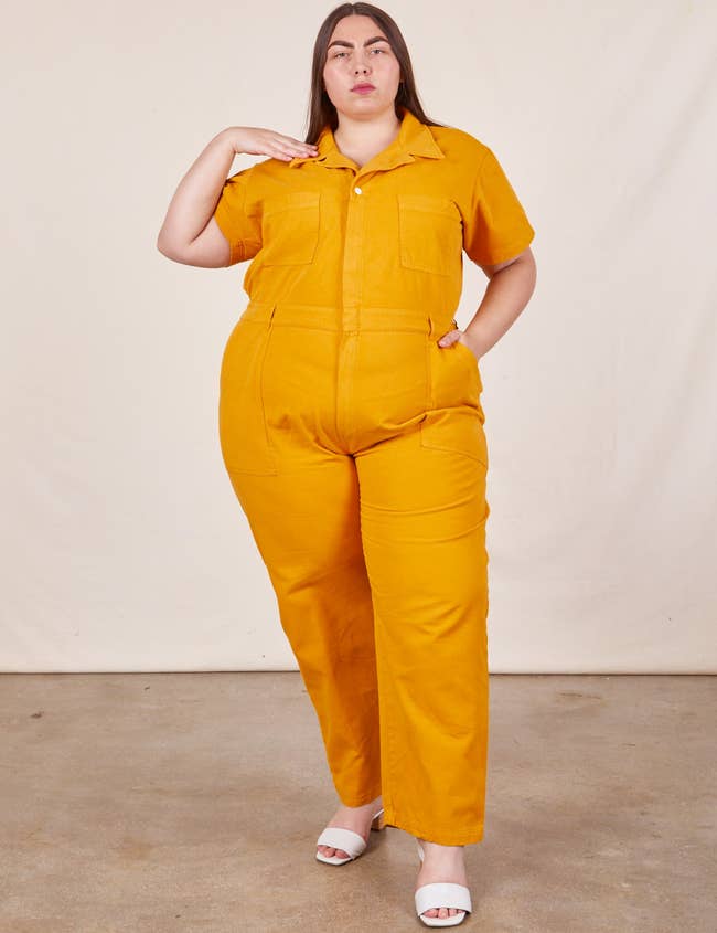 Person in a mustard yellow jumpsuit with front pockets standing confidently