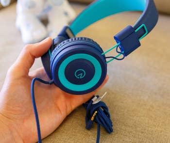 A reviewer holding the navy and teal colored headphones
