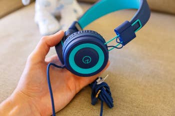A reviewer holding the navy and teal colored headphones
