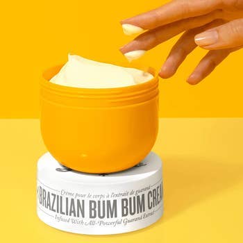 Model's manus  reaching into an unfastened  jar of Brazilian Bum Bum Cream