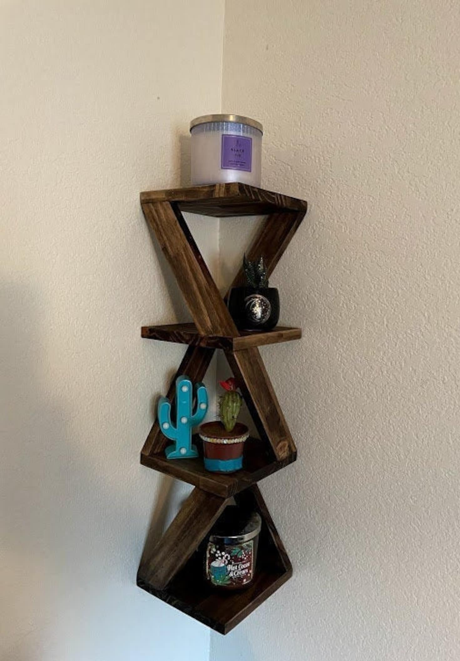 Brown twisty four-tier shelf hanging on corner of white wall with decor on top
