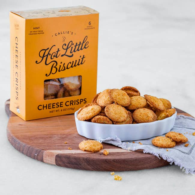 Box of Callie's Hot Little Biscuit Cheese Crisps and a vessel  of crisps displayed connected  a woody  committee  with a napkin