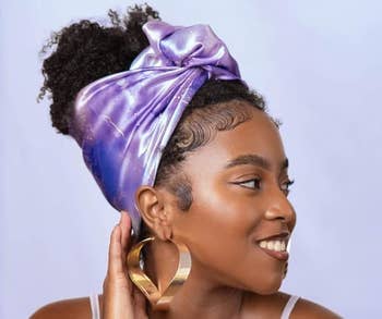 Model wearing a headwrap with hoop earrings, smiling and looking to the side