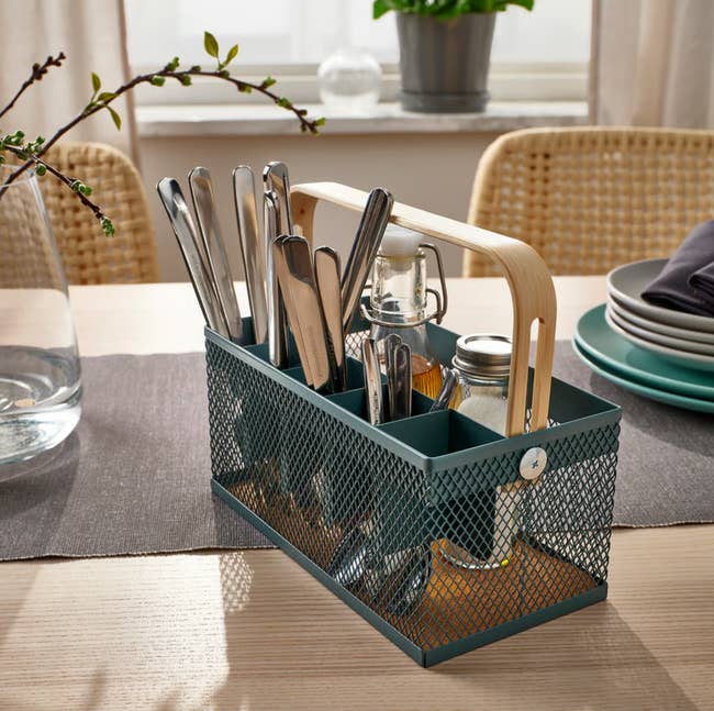Metal mesh cutlery caddy with a woody  grip  connected  a eating  table, holding utensils and tiny  jars, acceptable   for a casual repast  setting