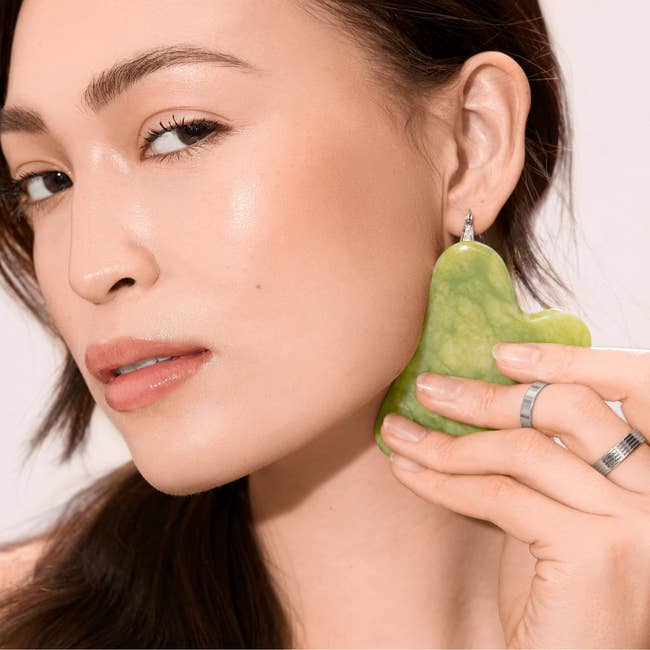 Person utilizing a heart-shaped jade facial massager connected  their face