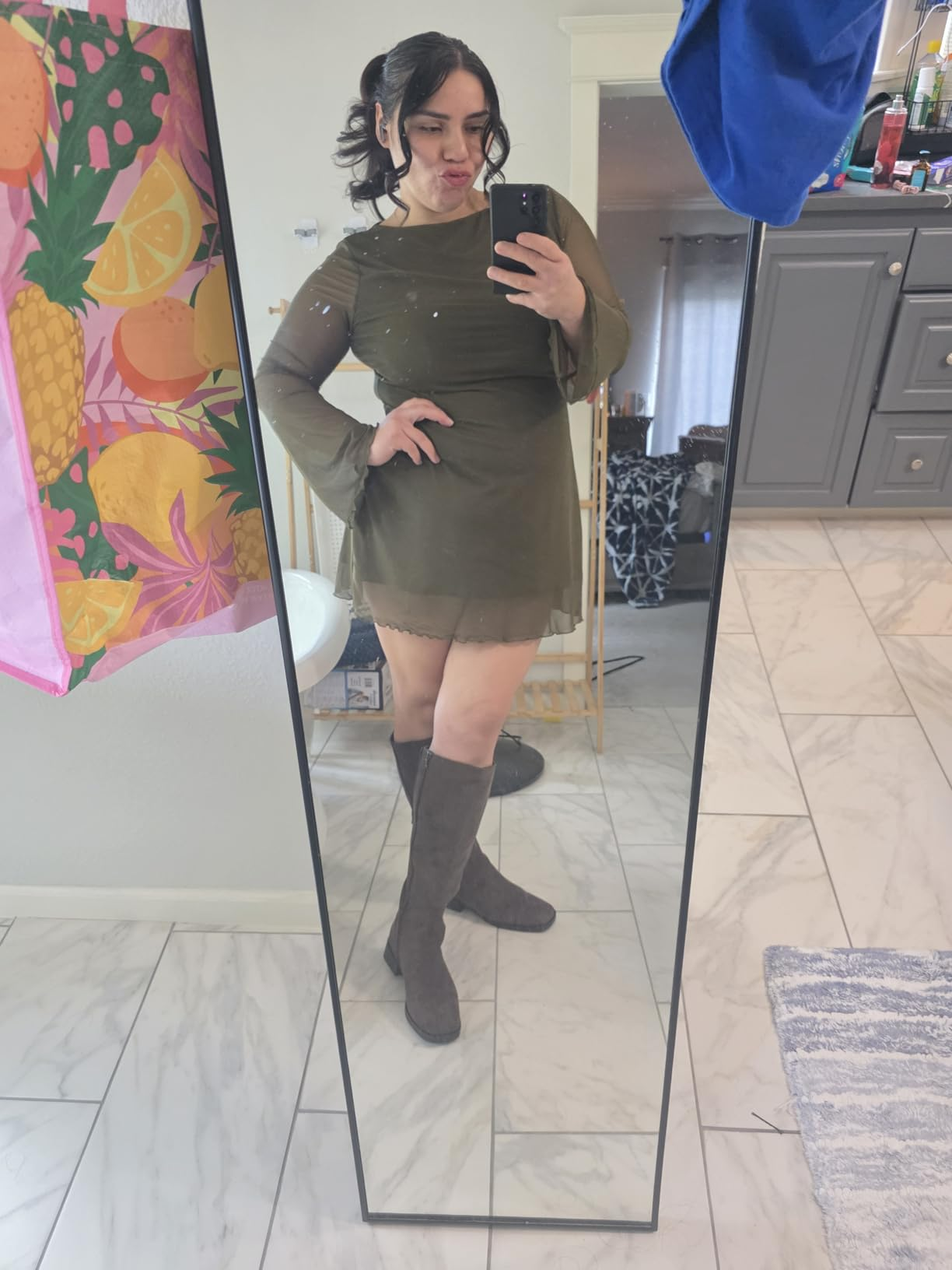Person successful  a reflector  selfie wearing a stylish bell-sleeve formal  and knee-high boots, lasting  connected  a tiled level  with colorful decor successful  the background