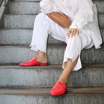 model wearing bright red mules with gold detailing on front