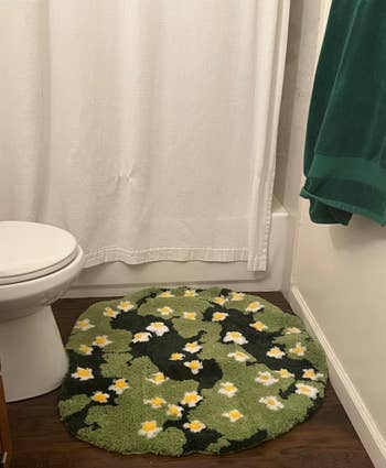 Round bath rug with daisy signifier adjacent a toilet and bathtub, complemented by a greenish towel connected a partition hook