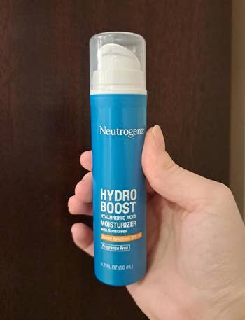 Hand holding a Neutrogena Hydro Boost Hyaluronic Acid Moisturizer with Sunscreen bottle. Fragrance-free, 1.7 fl oz size