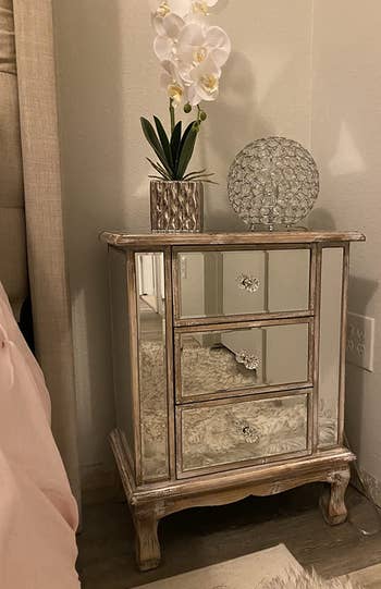 reviewer photo of rose gold mirrored nightstand with vase on it