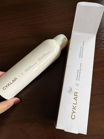 Person holding Cyklar Dry Shampoo vessel adjacent to its unfastened container connected a table