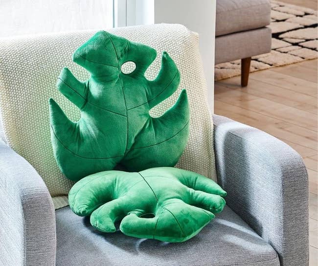 Two plush pillows shaped like green monstera leaves on a chair in a home setting
