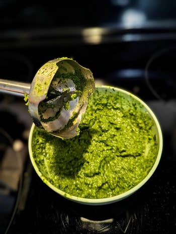 An immersion blender being lifted from a container of fresh pesto