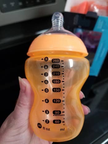 Person holding an orangish  babe  vessel  with measurement   markings successful  ounces and milliliters