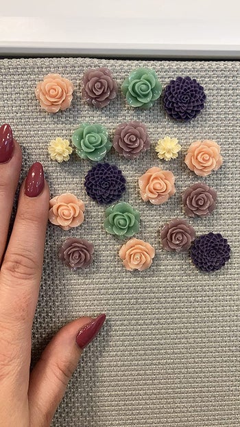 A reviewer's hand next to their purple floral pushpins that are stuck into their cubicle