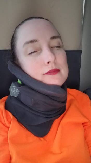 reviewer wearing black Trtl neck pillow on flight