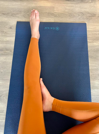 pic of me wearing orange workout leggings while stretching on the dark blue side of the yoga mat