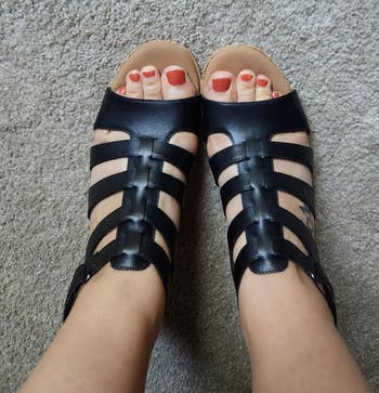 Feet wearing stylish achromatic  strappy sandals connected  a carpeted floor