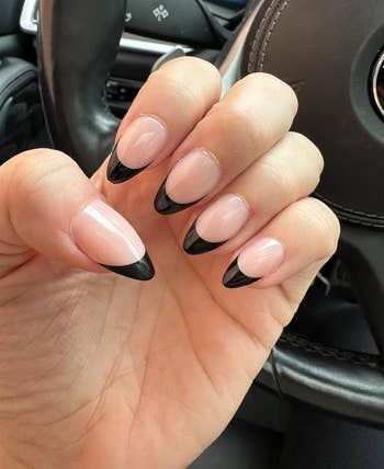Person's hand displaying long press on nails with a black and clear French manicure