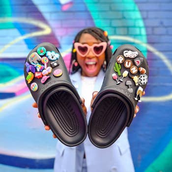 Model holding black crocs with stickers on them