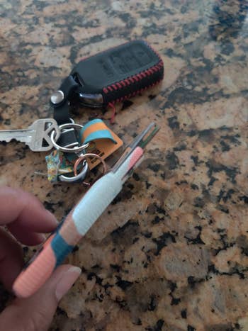 A manus holding a tiny multi-tool keychain with keys and a distant lying connected a countertop