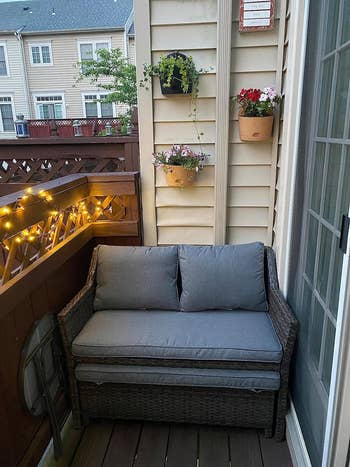 Outdoor patio setting with a loveseat and hanging plants, ambiently lit by string lights, for cozy home decor inspiration