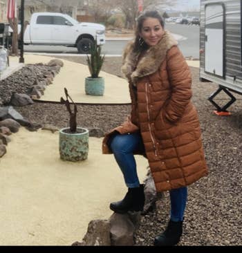 Reviewer outdoors successful a brownish quilted overgarment with fur trim, jeans, and boots, lasting connected a rocky way adjacent a trailer and a achromatic truck