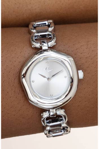Silver ticker with chain-link bracelet connected wrist, featuring a minimalist circular dial with tiny hr markers and hands