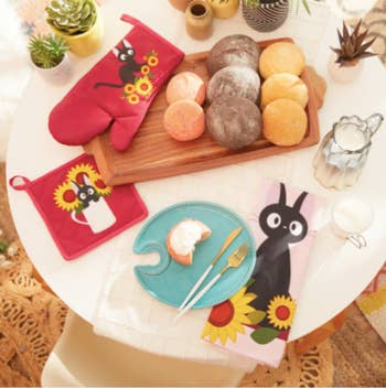 table with donuts and the red mitt and pot holder and light pink towel all featuring Jiji and sunflowers