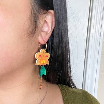 Person wearing a dangly orange orchid earring
