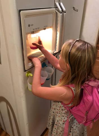 a reviewer's child using one of the cups to get water from a fridge door dispenser 