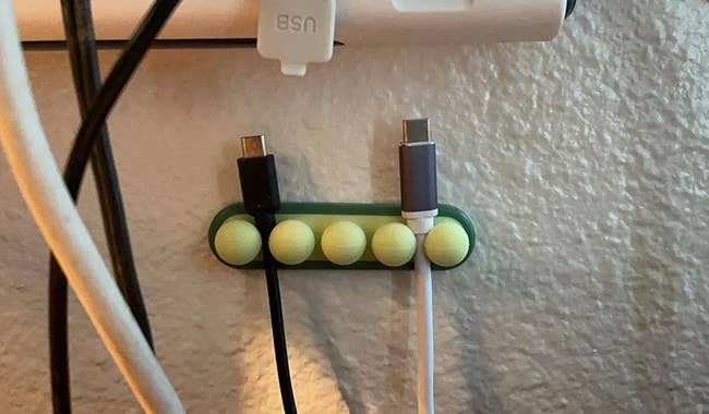 green pea pod cord organizer mounted to a wall with cables connected to it