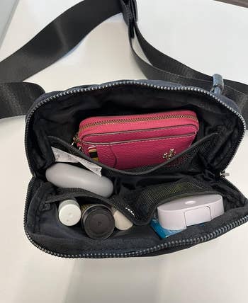 Open bag with various personal items including a wallet, electronic gadgets, and beauty products