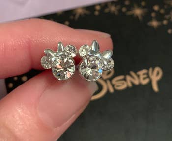 a reviewer holding two stud earrings shaped like minnie mouse