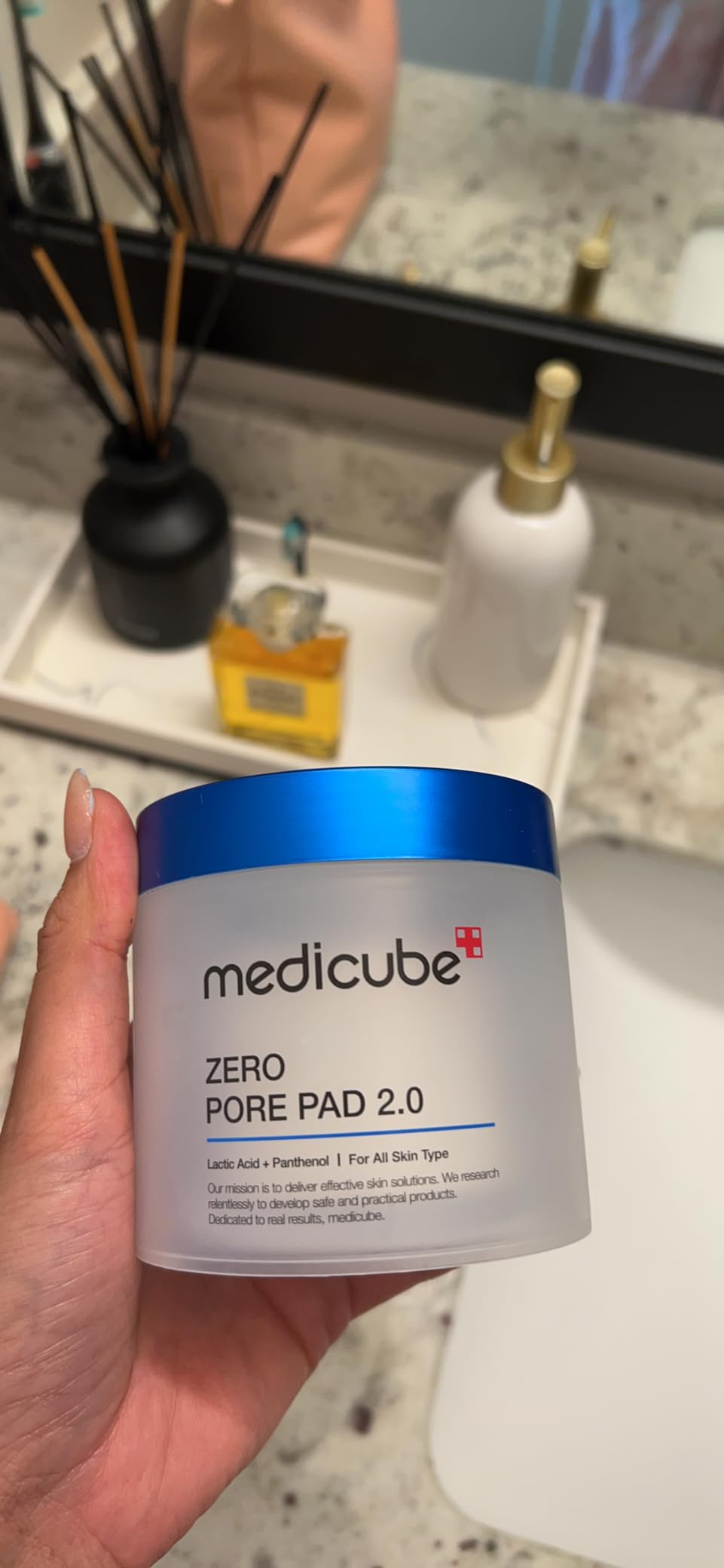 Person holding a Medicube Zero Pore Pad 2.0 instrumentality  successful  a bath  mounting  with a descend  and toiletries successful  the background