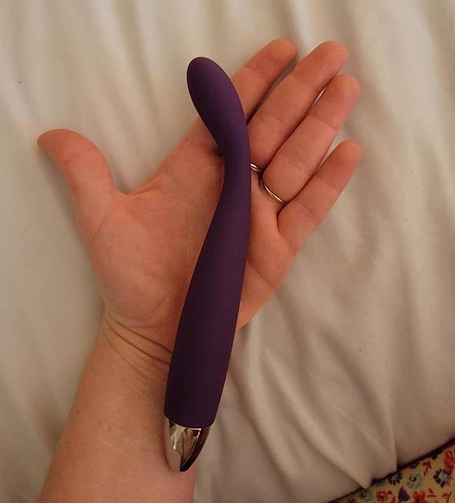 Reviewer holding purple slim G-spot vibrator on open palm