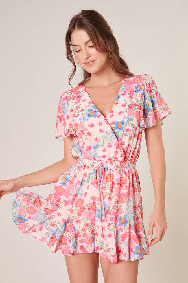 model in short sleeve surplice v neck romper in pink with floral print with flippy hem and drawstring waist
