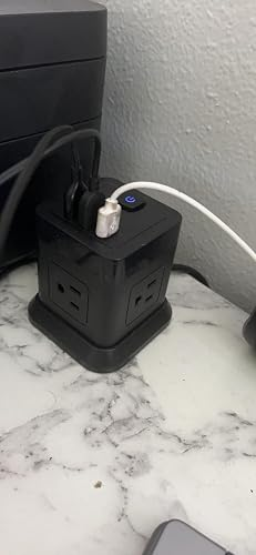 A black power strip tower with multiple outlets and USB ports sits on a marble surface, with several devices plugged in