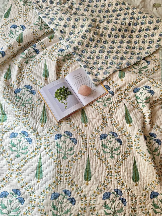 A floral-patterned quilt with a book and a stone placed on top, set up in a cozy and inviting manner, ideal for a relaxed reading session