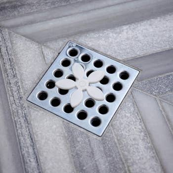 Decorative square shower drain with floral design, integrated into tiled floor