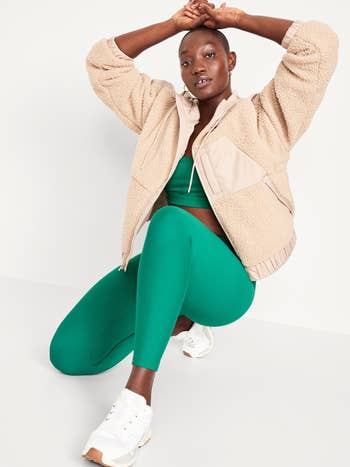 Model in a casual teddy jacket and green leggings sitting, hands behind head