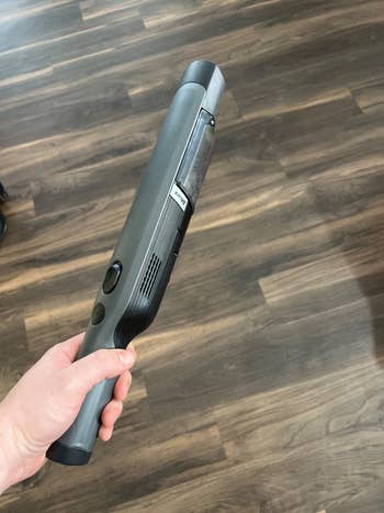 Hand holding a sleek, modern handheld vacuum cleaner with a streamlined plan connected a wood level background